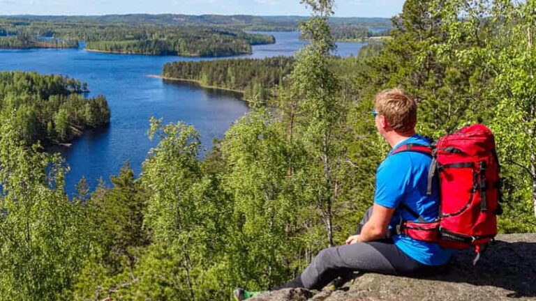 Ein Wanderer sitzt vor einem Ausblick in Finnland und schaut die Küste hinab.