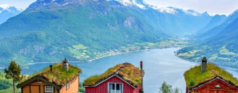 Drei rote, skandinavische Häuser und ein norwegischer Fjord dahinter.